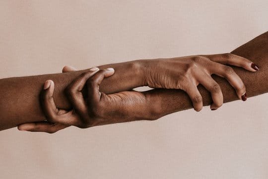 A stock picture of two black hands holding each other. The hands are gripping each others arms