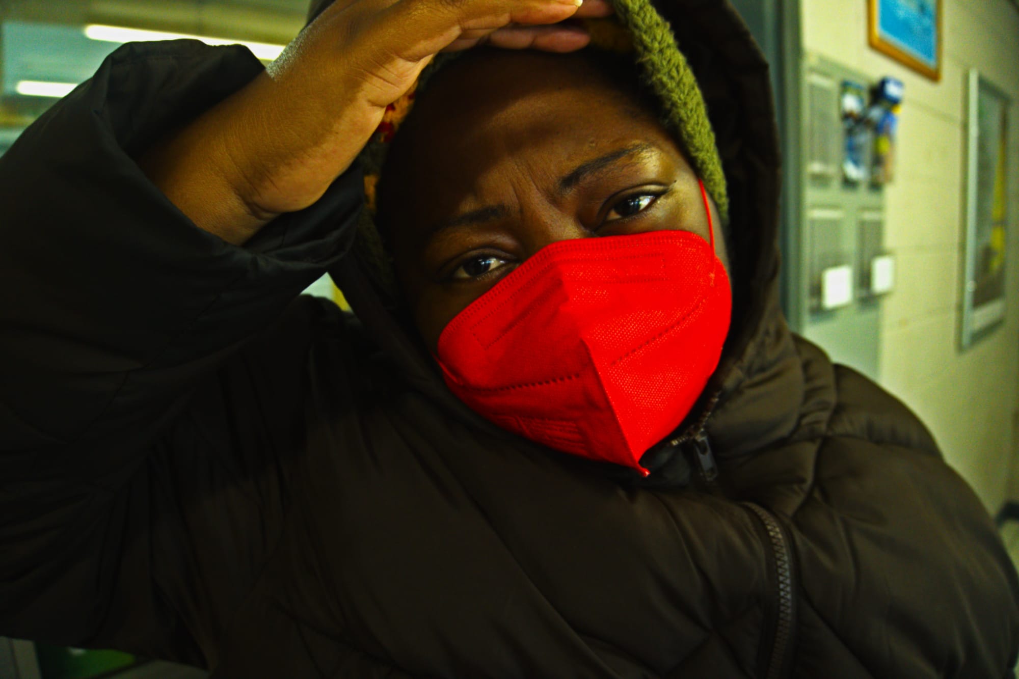 A dark skin African in a red mask and brown coat in a train station