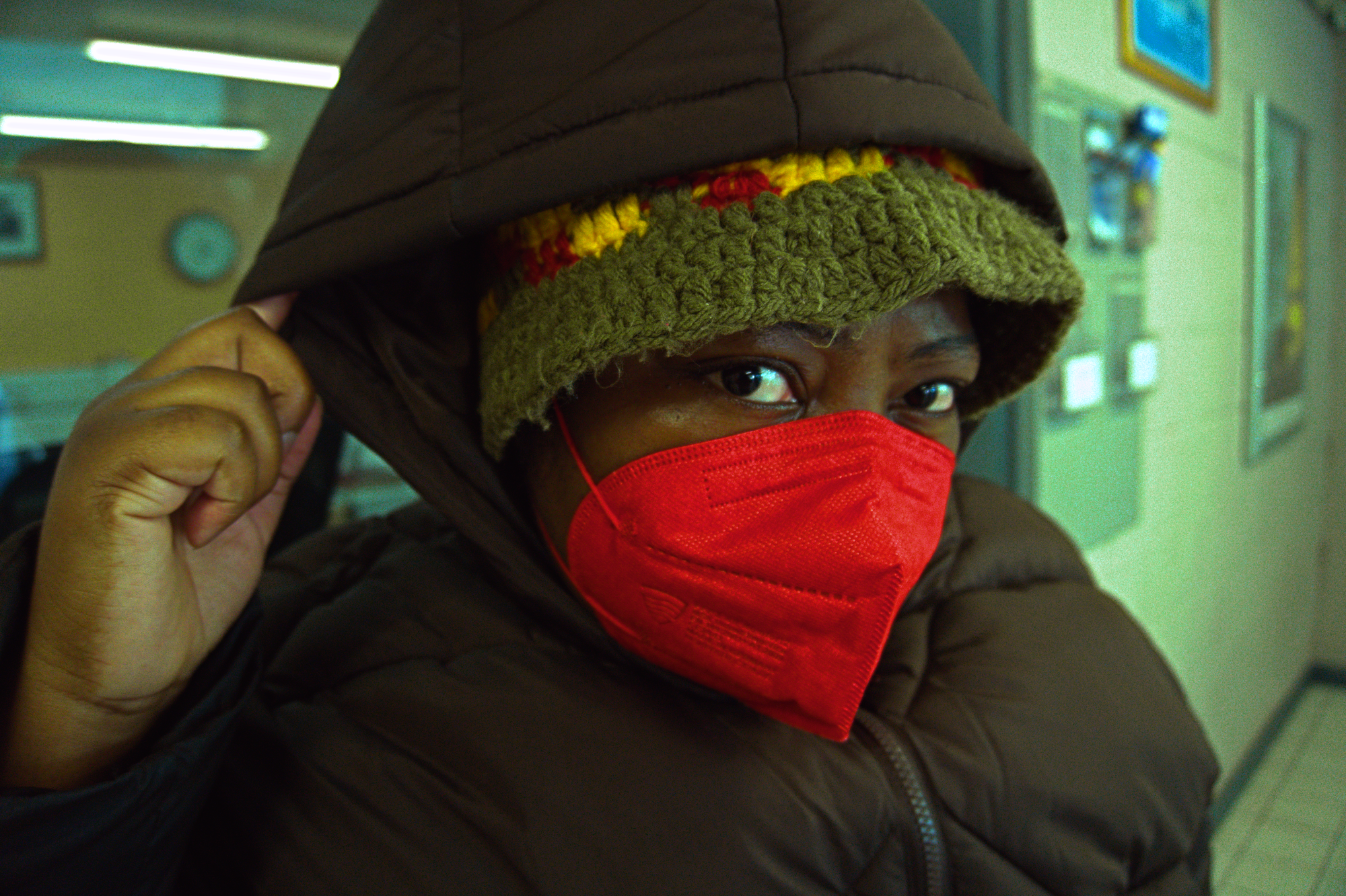 A dark skin African in a red mask and brown coat in a train station