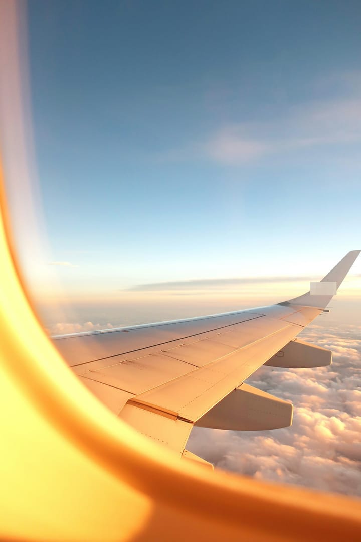 An image of the  from an aeroplane window view, overlooking clouds and the wing of the plane, image has a golden hue. 